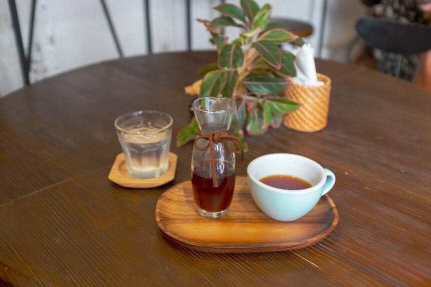 Coffee display on a wooden table. Glass carafe and ceramic cup on a wooden tray with a glass of water and a plant in the background